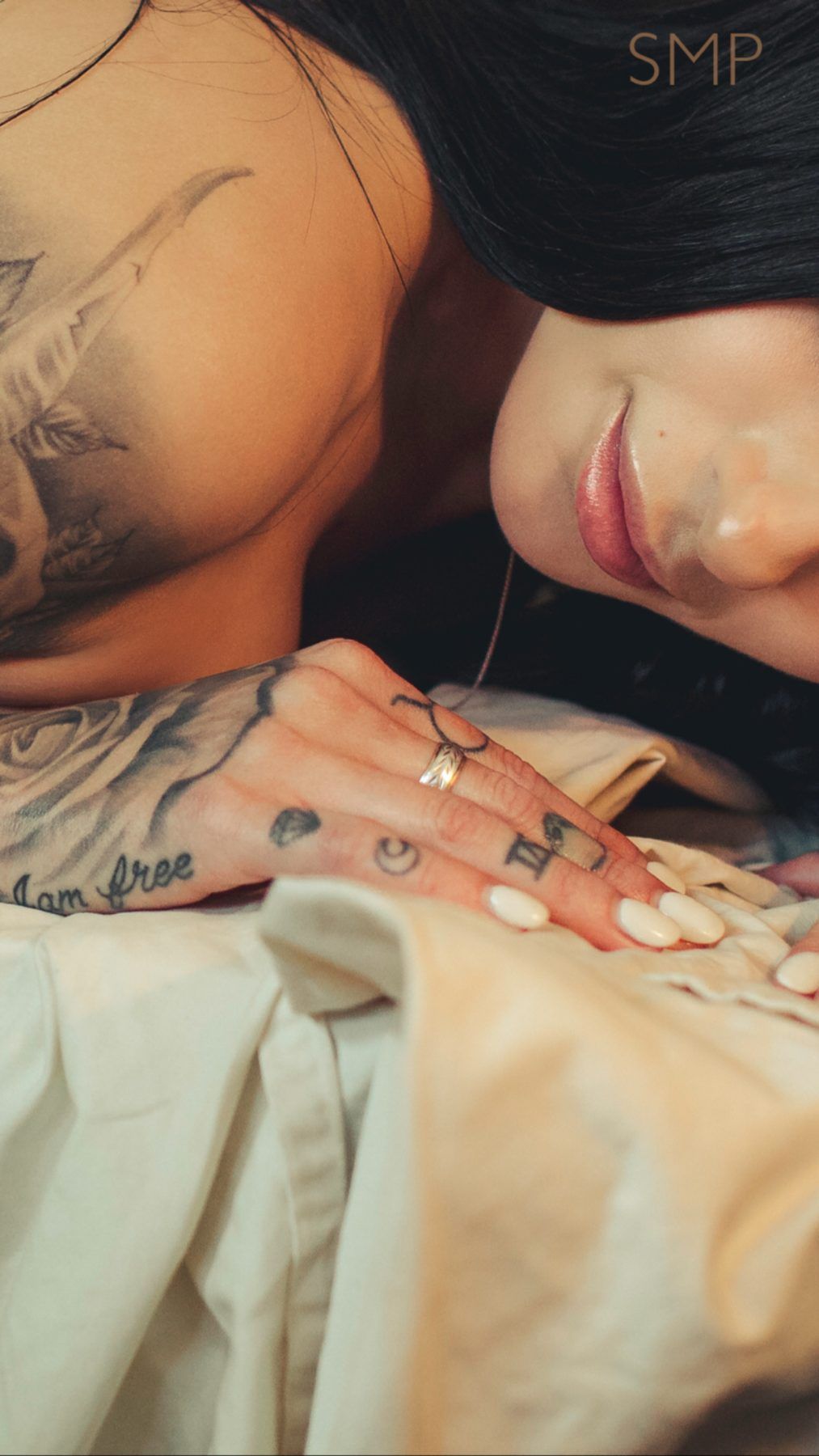 Tattooed woman resting her head on her arm on white sheets